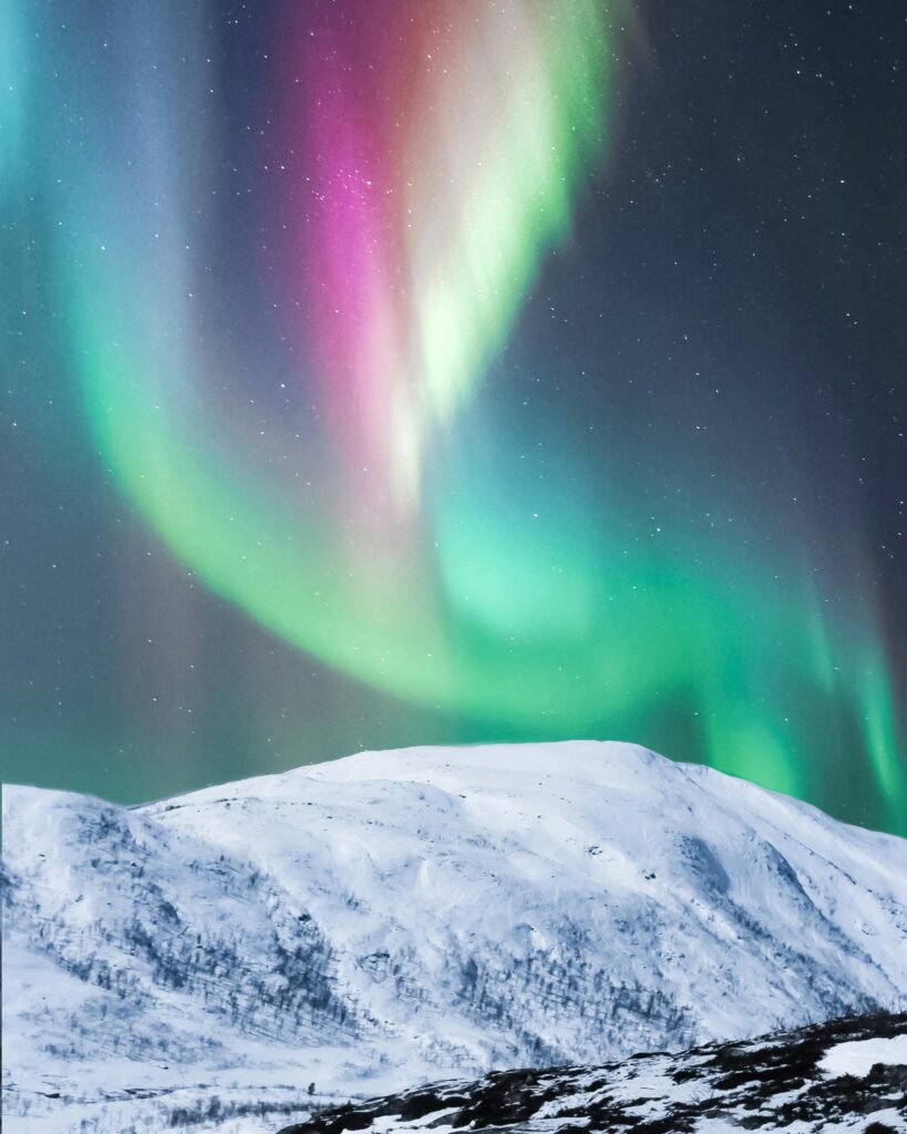 Colorful aurora borealis dancing over snowy hills in Senja, Norway, creating a breathtaking night scene.